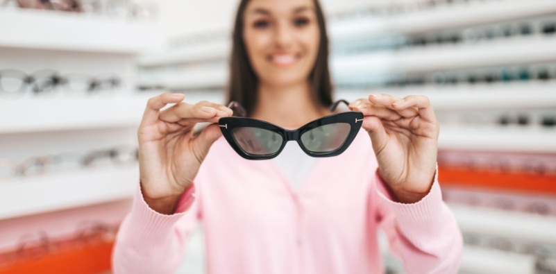 A woman holding up a pair of sunglasses in the opticians practice