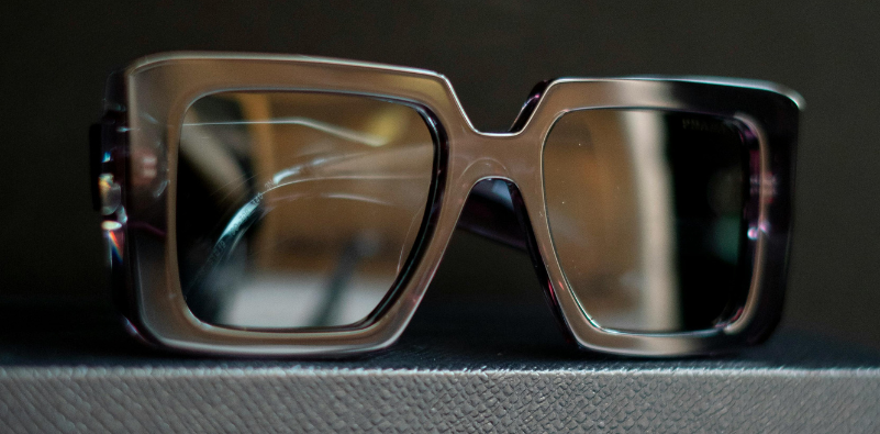 A pair of black square oversized sunglasses on a textured surface.