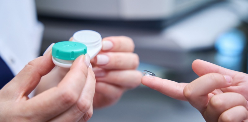 Optician handing contact lens to patient