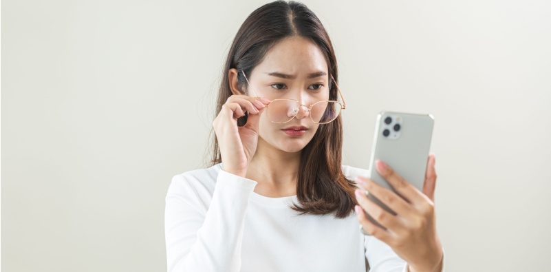 woman adjusting glasses to see her phone clearly