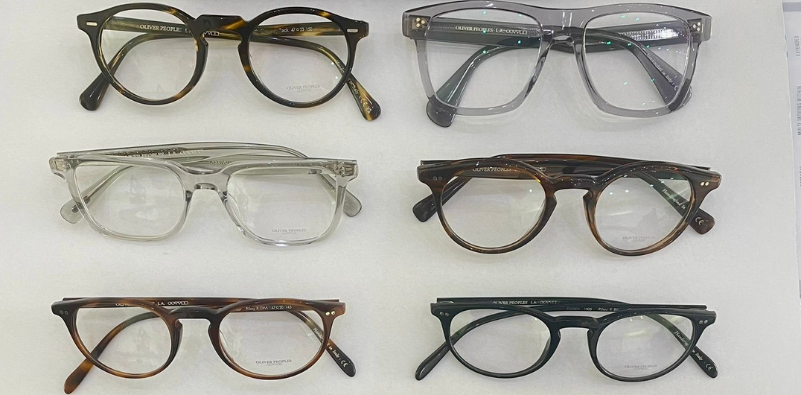 A selection of Oliver Peoples eyewear in a variety of styles and colours, taken from above on a white background.