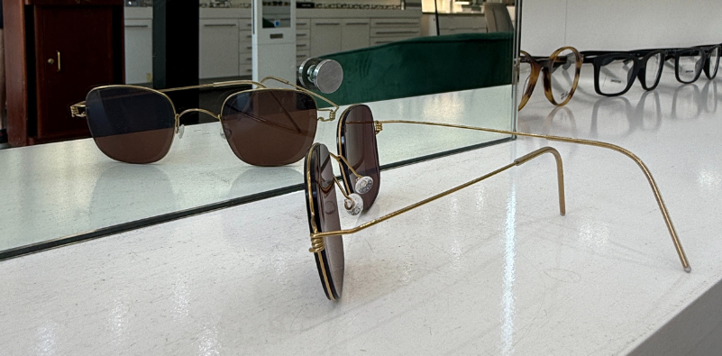 A close-up photo of a pair of gold LINDBERG sunglasses with brown lenses facing towards a mirror.
