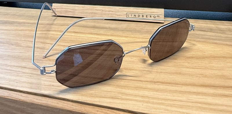 A pair of silver geometric LINDBERG sunglasses with brown lenses on a wooden surface.