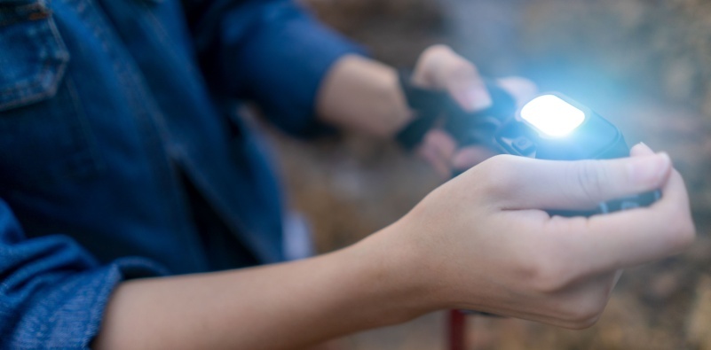 A close up of a hiker holding a lit head torch in their hands.