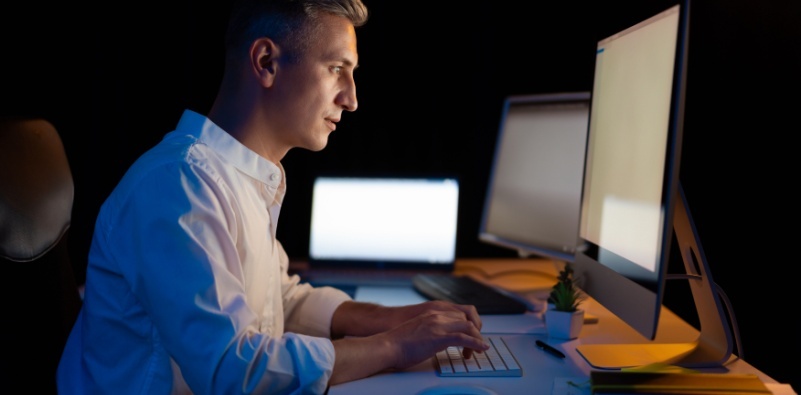 A focused man working on a computer in a dark office.