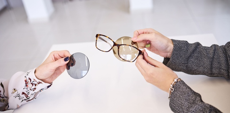 An optician showing a patient the difference between grey and brown tinted lenses against a brown tortoiseshell frame.