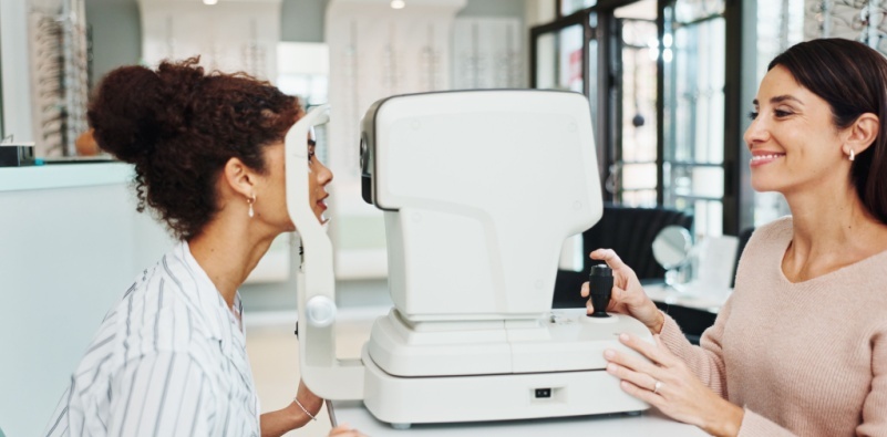 A young woman having a test carried out on a piece of equipment at the opticians by a female member of the team