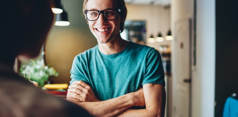 A middle aged man wearing a pair of black glasses, talking to a colleague.