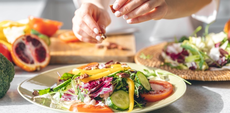 A close-up of a woman’s hands making a fresh vegetable salad