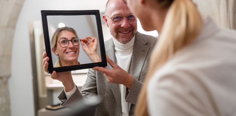An optician holding up a mirror to a woman trying on glasses