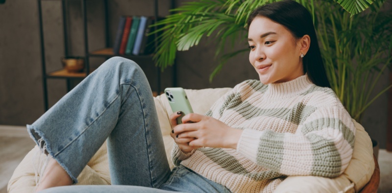 A young woman wearing casual clothing, sat in an armchair looking at her mobile phone