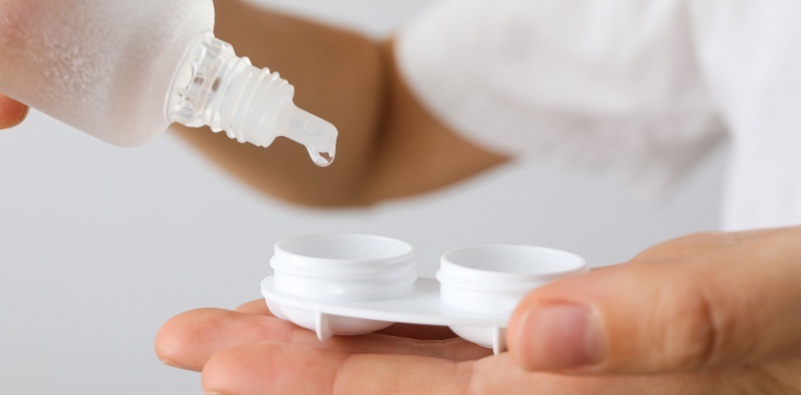 A close-up of a man putting contact lens solution into a contact lens storage container