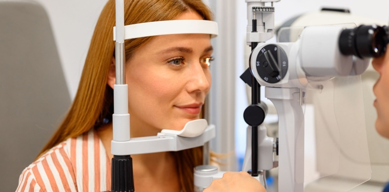 A young, red haired woman wearing a striped shirt, having an eye exam at the opticians
