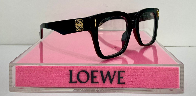 A pair of bold black LOEWE glasses on a pink LOEWE display block at Optikal Opticians