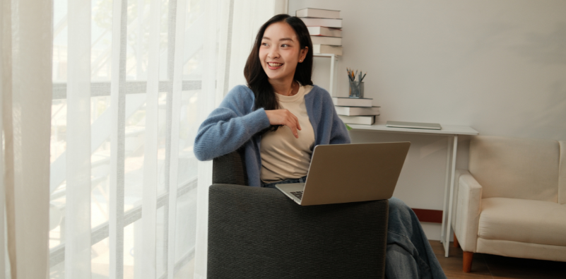 Woman smiling looking through window with a laptop in a bright home office