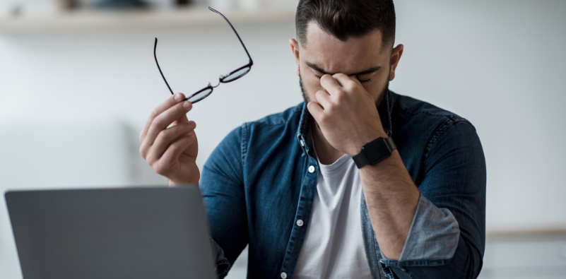 Man holding his glasses and rubbing tired eyes at a laptop