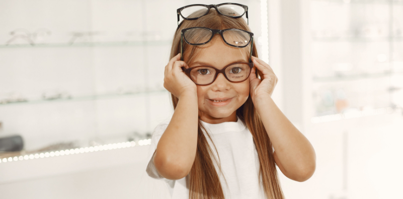 Smiling child trying on several pairs of glasses